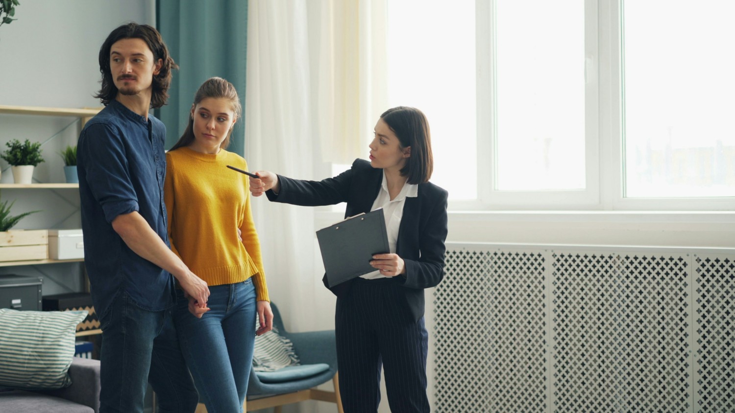 Landlord confronting tenants inside rental apartment, holding clipboard and pointing while couple listens.