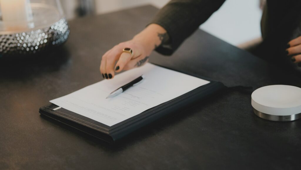 Person reaching for a rental agreement on a clipboard with a pen on a dark table.