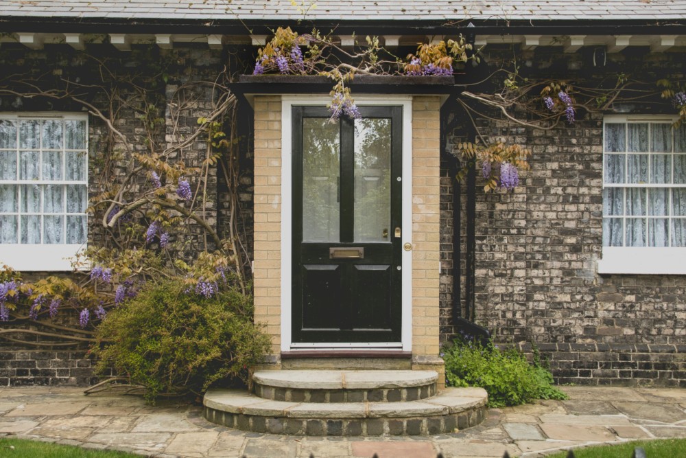 Front entrance of a brick house with flowering vines and a black door, representing residential property or home exterior.