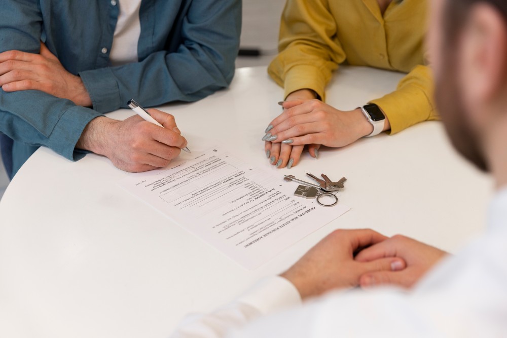 Tenant signing rental agreement with landlord, lease contract and apartment keys visible on table.