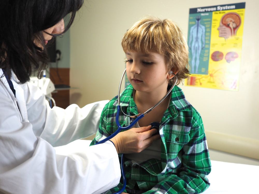 Doctora usando un estetoscopio para escuchar el pecho de un niño durante un examen médico.