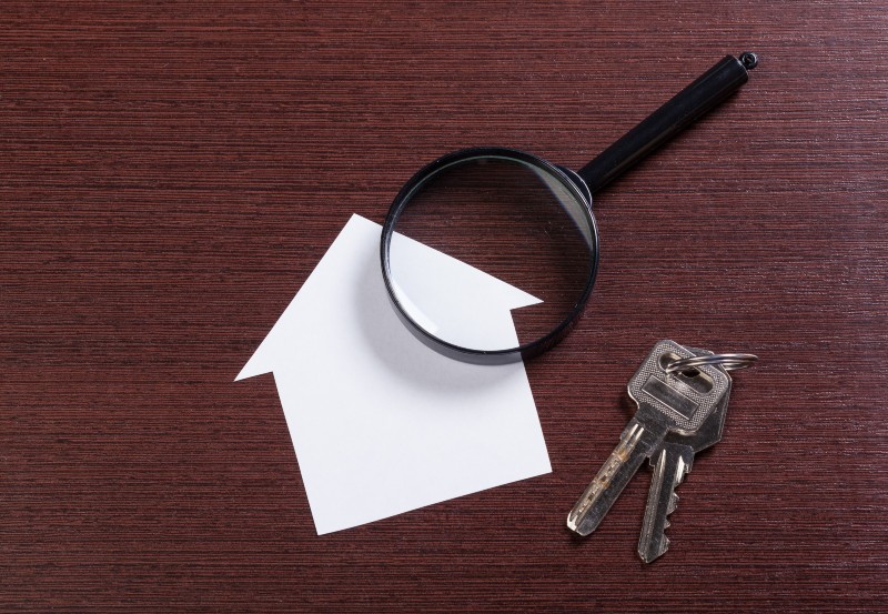 Magnifying glass over house icon next to keys, representing landlord review of rental history before lease approval.