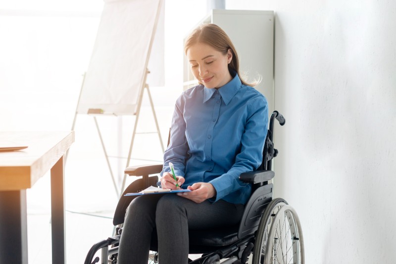 Woman in wheelchair filling out rental paperwork, representing disabled tenants’ rights and housing accessibility.