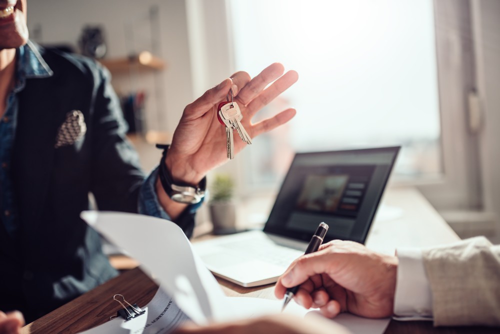 Tenant signing rental agreement while landlord or property manager holds house keys.