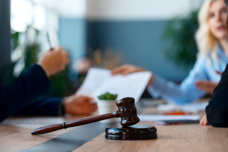 Close-up of gavel on lawyer’s desk with people discussing documents in the background.
